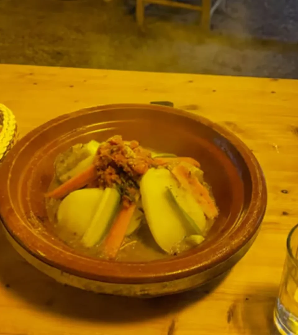 A hearty Moroccan tagine with vegetables and fresh bread, served during the Agafay Desert dinner show, accompanied by a glass of water.