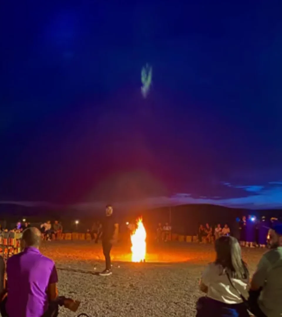 Guests enjoying an Agafay Desert dinner show, watching a fire performance under the starry night sky.