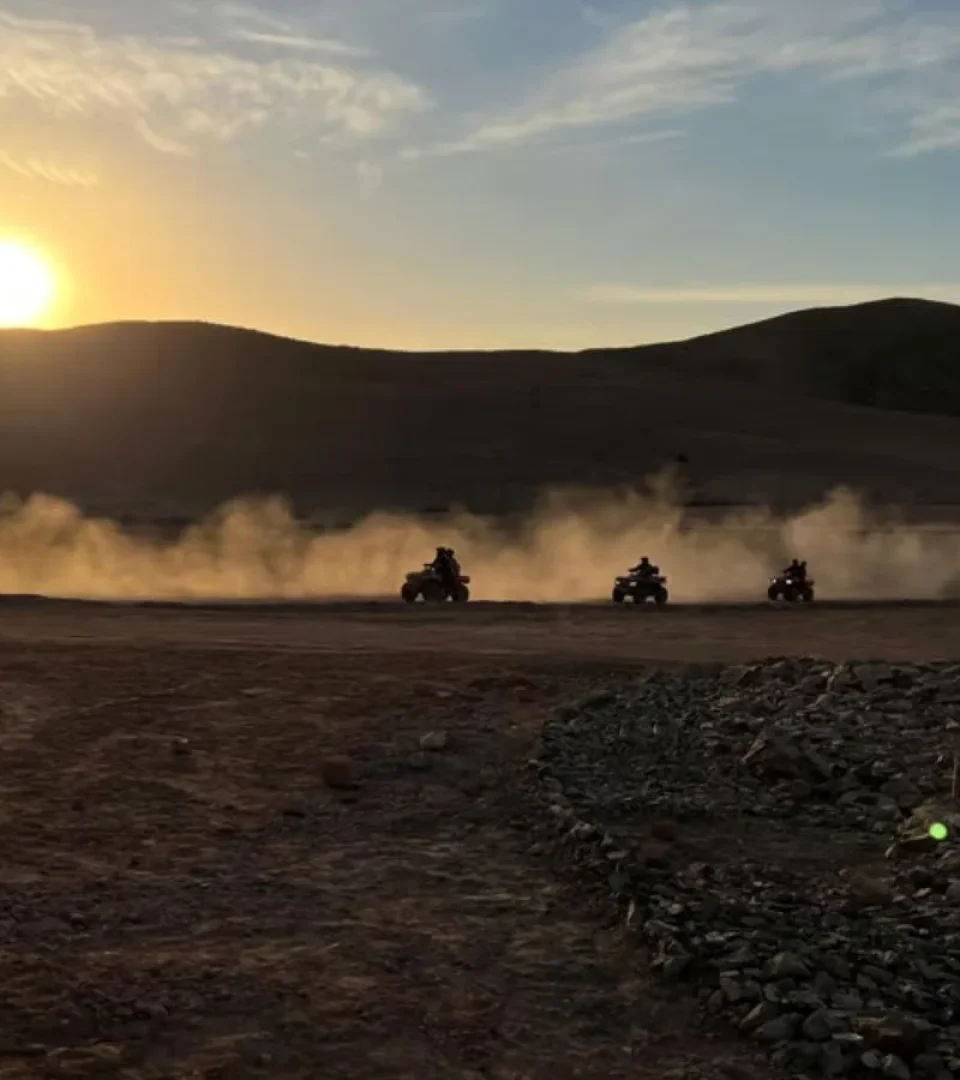 Riders on a quad bike tour in Agafay Desert, kicking up dust at sunset before an enchanting dinner show with camels.