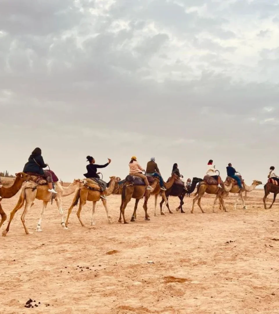 Travelers enjoy a Marrakech Agafay Desert dinner in a Berber camp and camel ride, exploring the vast desert under a cloudy sky.