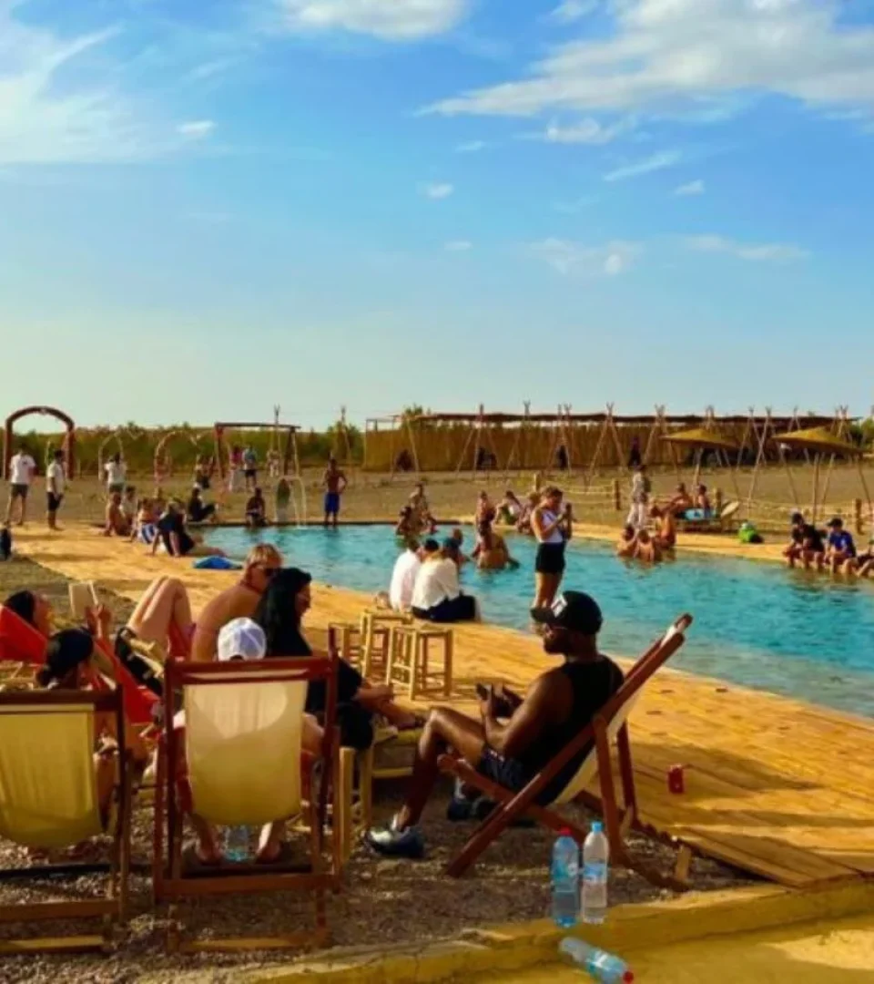 People relaxing at an Agafay Desert swimming pool, enjoying the sun, refreshing water, and scenic desert surroundings.