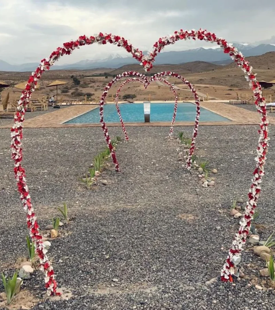 A beautifully decorated Sahara luxury camp with heart-shaped floral arches leading to a stunning pool in the desert.