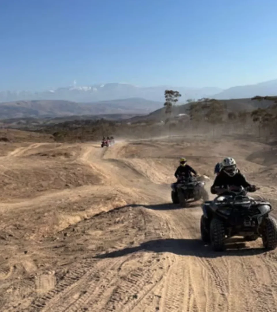 Riders on an Agafay Desert quad bike tour, kicking up dust as they navigate scenic desert trails with mountains in the background.
