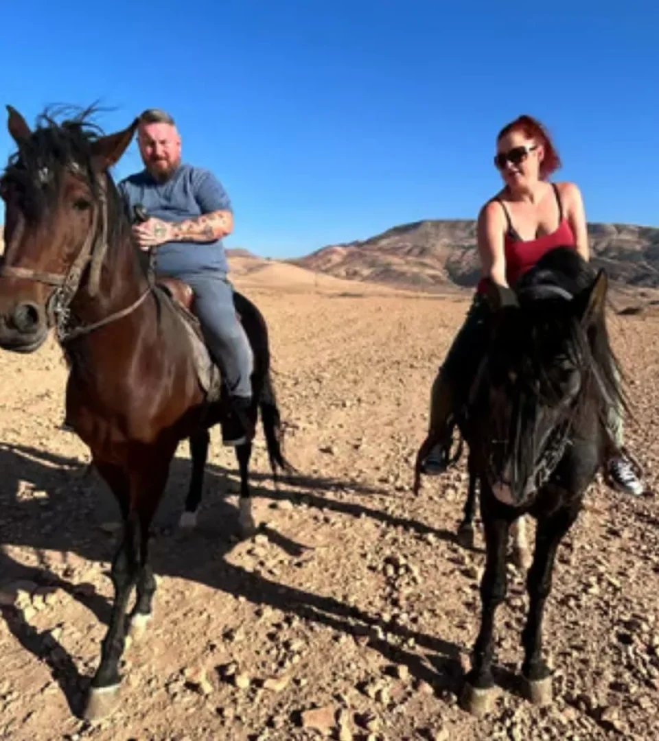 Two riders enjoying a horse riding Marrakech experience, exploring the scenic desert terrain under a bright blue sky.